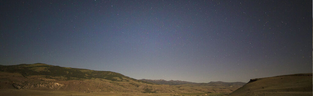 A night sky over a valley with mountains in the background.